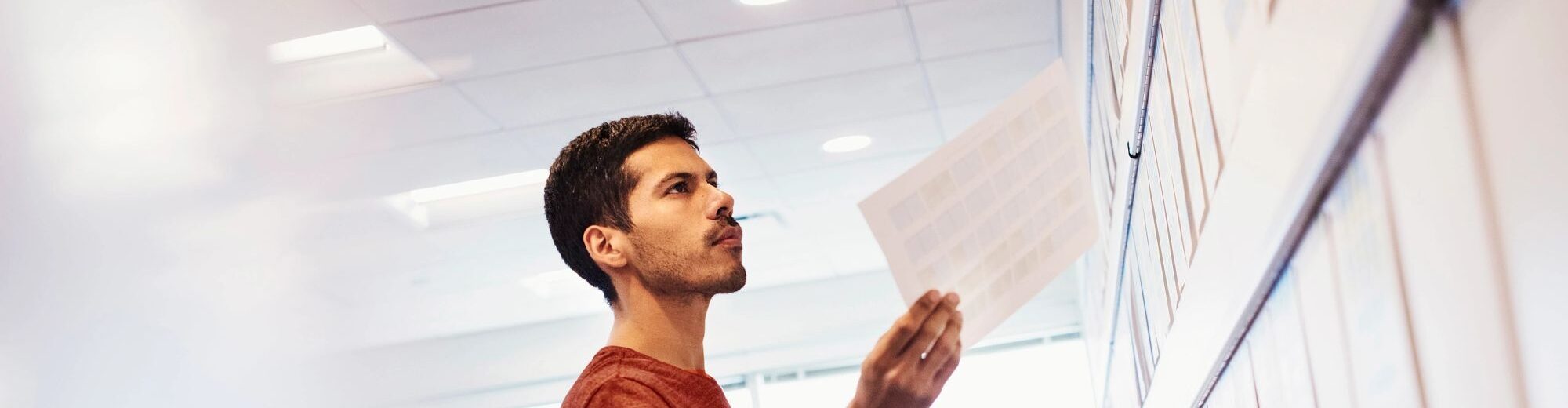 Woman and man standing in office adding paper to display wall 696155891